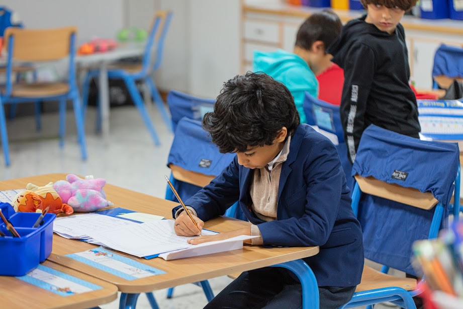 A boy in a school uniform focused on writing on a piece of paper.